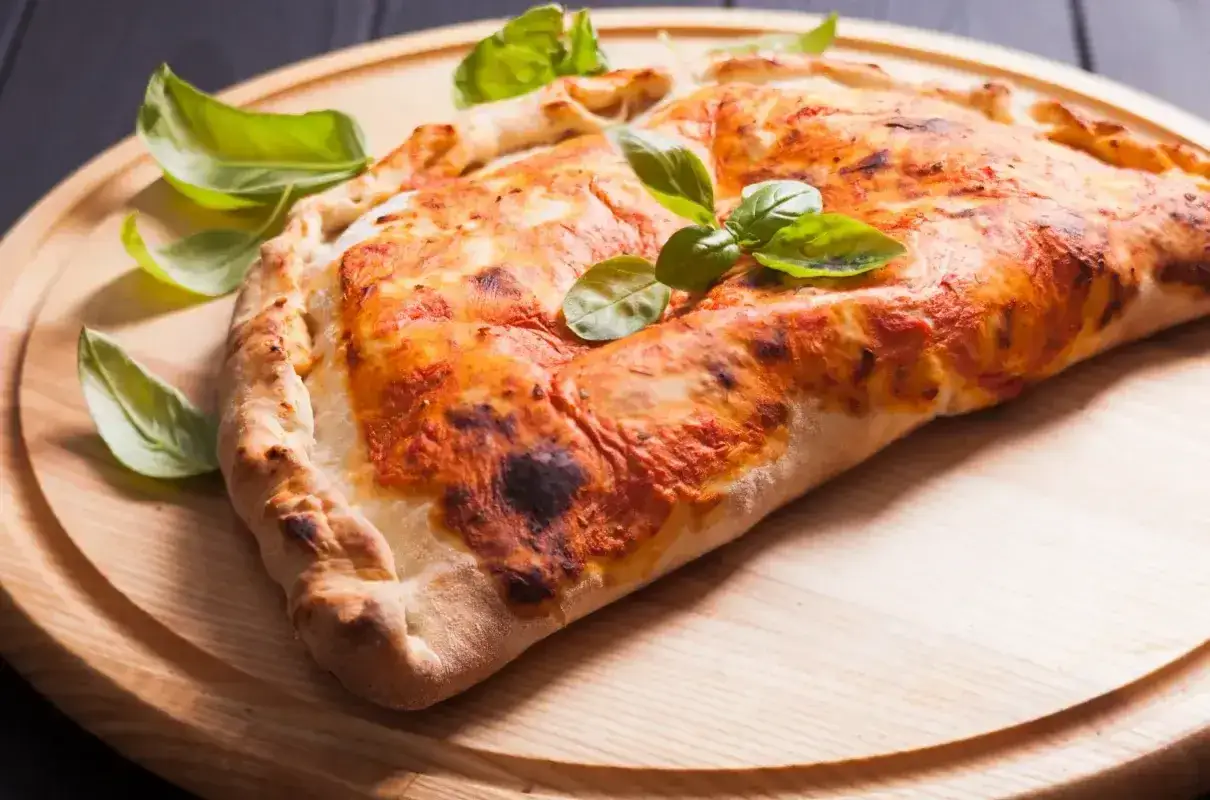 Złocisty calzone z sosem pomidorowym i serem, ozdobiony listkami bazylii. Pyszna przekąska, której calzone kcal nie są aż tak straszne.