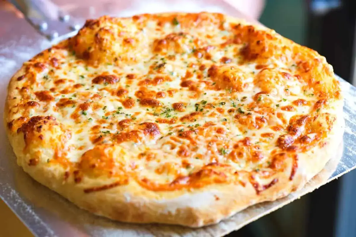 Gorąca, apetyczna pizza z samym serem, z rumianymi brzegami i posypką z ziół. Idealna na szybki posiłek.