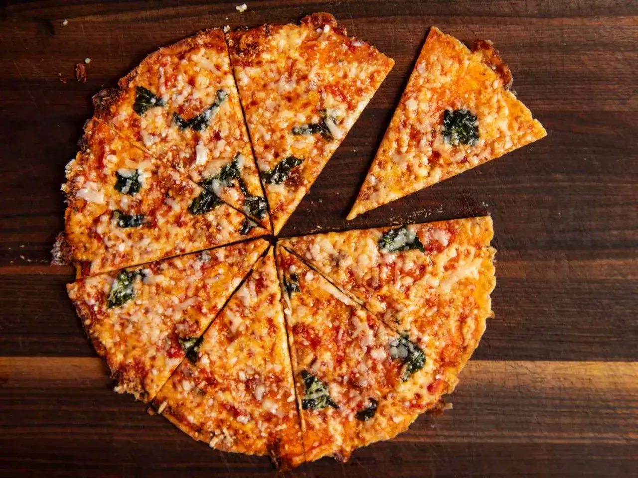 Chrupiąca pizza z tortilli, pokrojona na kawałki, z roztopionym serem i zielonymi listkami bazylii, prezentuje się apetycznie na drewnianej desce.