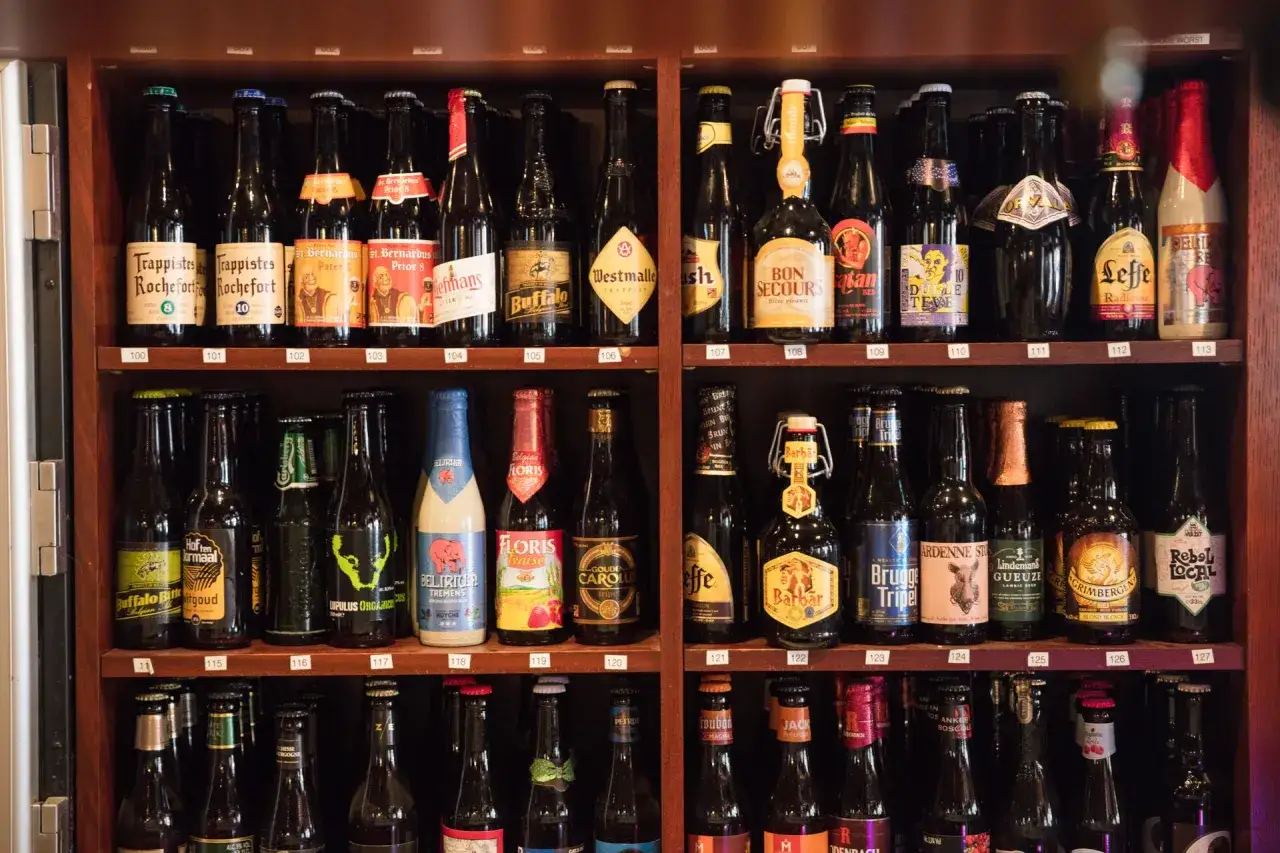 Rządki regał pełen butelek belgijskiego piwa, od klasycznych Trappistów po nowoczesne krafty.