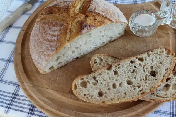 Chleb żytni na zakwasie, przekrojony na desce, z kilkoma kromkami i solniczką.