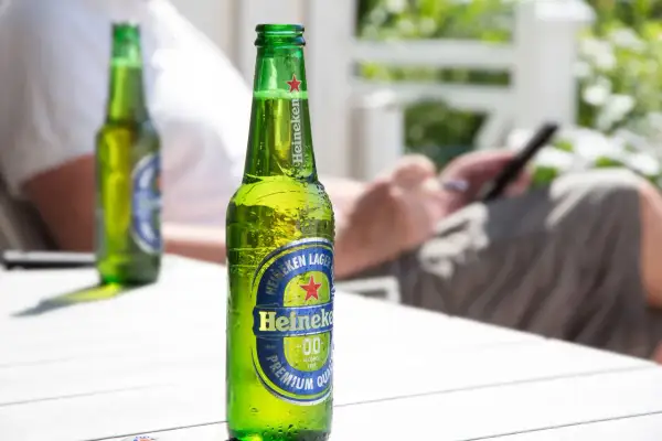 Orzeźwiająca butelka Heineken 0.0 procent, idealna na letni relaks. W tle osoba korzystająca z telefonu.