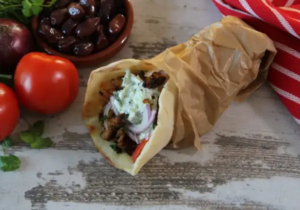 Pyszny pita gyros z soczystym mięsem, warzywami i kremowym sosem, obok pomidory, oliwki i cebula.