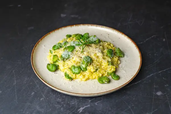 Risotto z bobem i parmezanem, jedno z pysznych włoskich dań głównych, udekorowane gałązką rozmarynu.