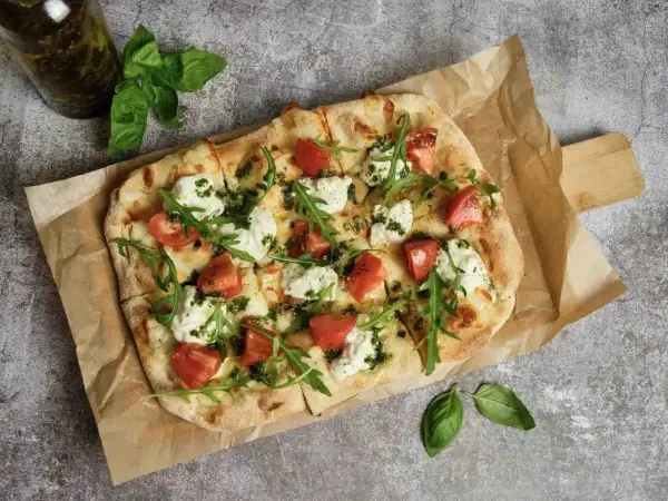 Pyszna pizza wege z pomidorami, mozzarellą i rukolą, polana zielonym pesto. Idealna na lekki posiłek.