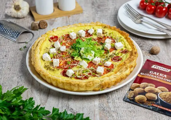 Tarta z pomidorami i kostkami sera mozzarella starta, ozdobiona kiełkami i ziołami.