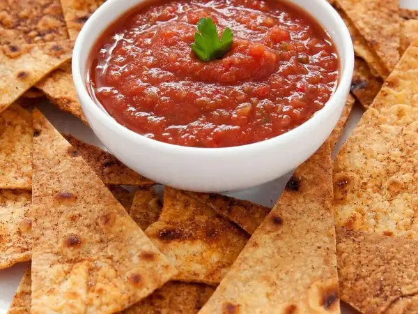 Chrupiące nachos otaczają miseczkę z aromatyczną, domową **salsą pomidorową**, ozdobioną listkiem pietruszki. Idealna przekąska!