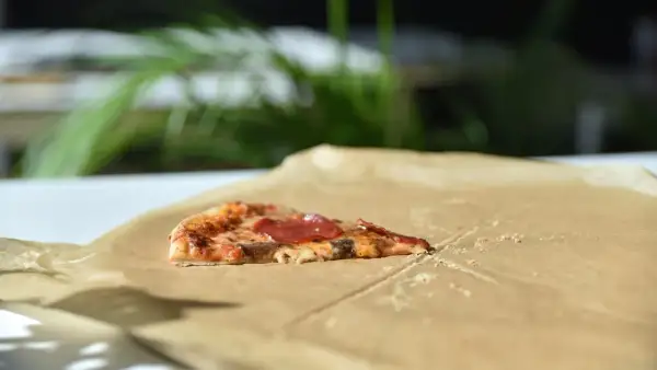Kawałek pizzy z salami na śniadanie, leżący na papierze do pieczenia.