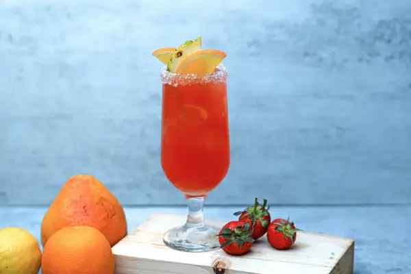 Orzeźwiający drink z pomarańczy i ananasa, z solą na brzegu kieliszka. Obok leżą truskawki, cytryna i pomarańcza. Idealny na lato, jak piwo cytrynowe.
