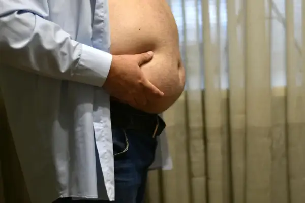 Mężczyzna z dużym brzuchem od piwa, trzymający się za brzuch.