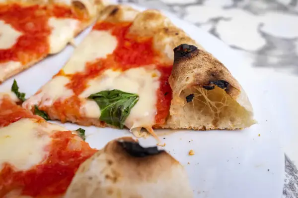 Kawałki pysznej pizzy neapolitańskiej z ciągnącym się serem i świeżą bazylią.