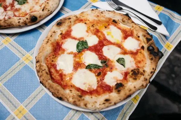 Pyszna pizza z samym serem, pomidorami i bazylią, z chrupiącym, lekko przypalonym brzegiem, na niebiesko-żółtym obrusie.