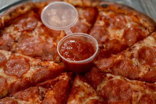 Pizza pepperoni z małym kubeczkiem sosu. Czy wolisz keczup czy ketchup?