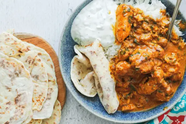 Pyszny kurczak butter masala z ryżem, jogurtem i chlebkami naan.