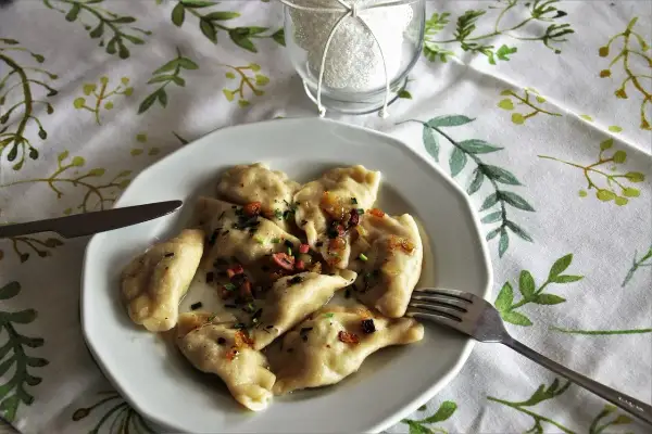 Pyszne pierogi Ania gotuje, polane skwarkami i szczypiorkiem. Na talerzu obok widelca i noża.