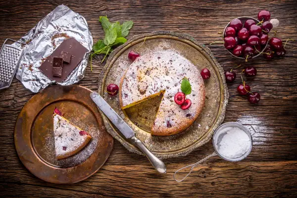Pyszny kawałek ciasta drożdżowego z wiśniami, posypany cukrem pudrem. Idealny deser, choć warto pamiętać o jego kcal.