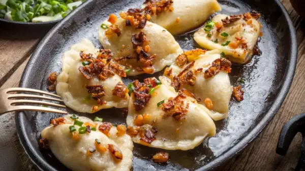 Pyszne pierogi z mięsem mielonym, okraszone skwarkami i szczypiorkiem, podane na żeliwnej patelni.