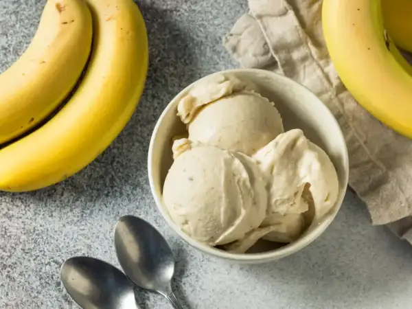 Pyszne lody bananowe w miseczce, obok świeże banany i łyżeczki. Idealne na upalny dzień.