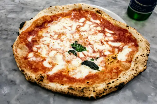 Nietypowa pizza margherita z lekko przypalonymi brzegami i świeżą bazylią, prezentująca się apetycznie na marmurowym blacie.