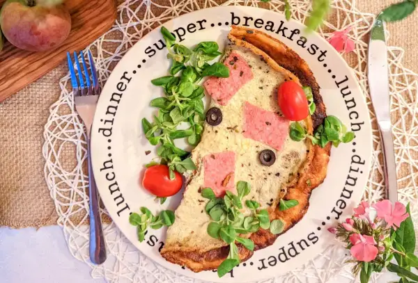 Pyszne, sycące śniadanie do pracy: omlet z szynką, pomidorkami i oliwkami, udekorowany świeżą sałatką.