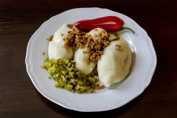 Gotowe kartacze na talerzu, posypane skwarkami, z ogórkiem kiszonym i papryczką chili. Idealne do podania według przepisu na kartacze.