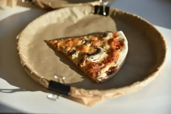 Kawałek pizzy z pieczarkami na papierowym talerzu. Zastanawiasz się nad ciasto na pizze kcal?