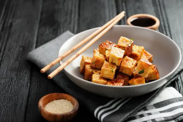 Kostki smażonego tofu, z którego jest tofu, w sosie, pałeczki, sezam i sos sojowy na ciemnym tle.