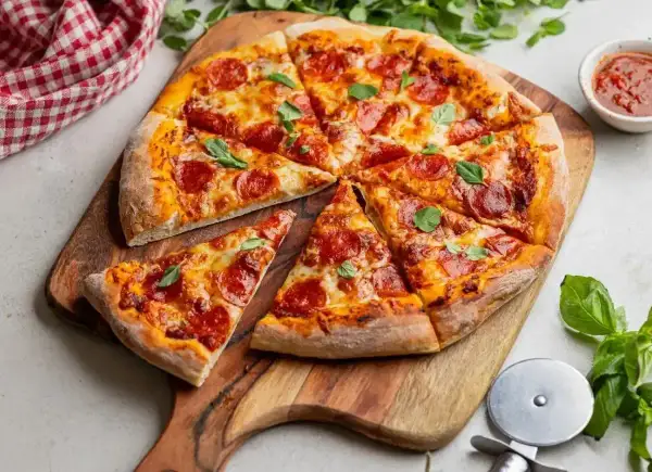 Pyszna pizza pepperoni, idealna na ostro, z ciągnącym się serem i świeżą bazylią, podana na drewnianej desce.